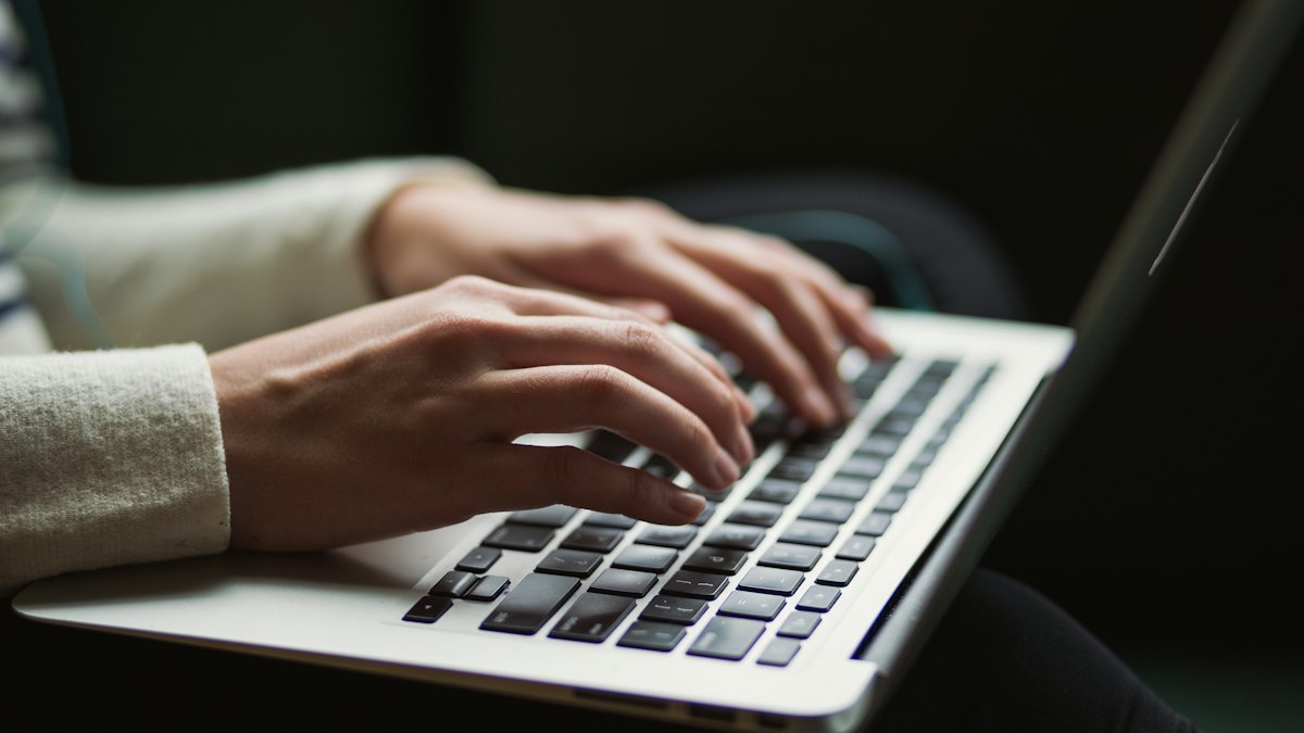 Hands typing on a laptop keyboard in a dark room
