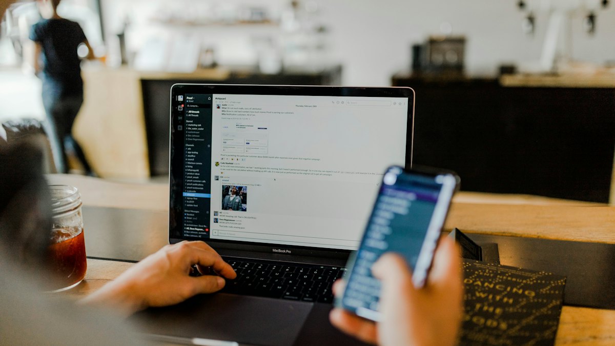 Person using a phone in front of a laptop